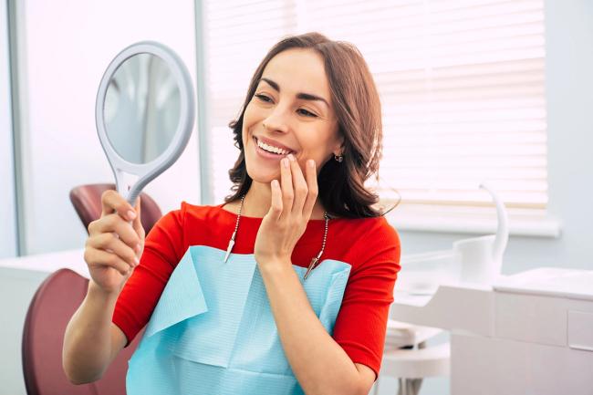 a woman is looking at her teeth in a mirror at the dentist .