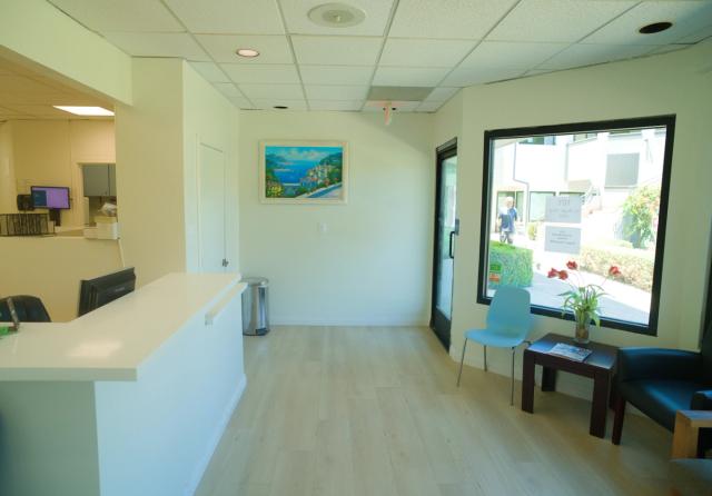 a waiting room with a desk , chairs , tables and a painting on the wall .