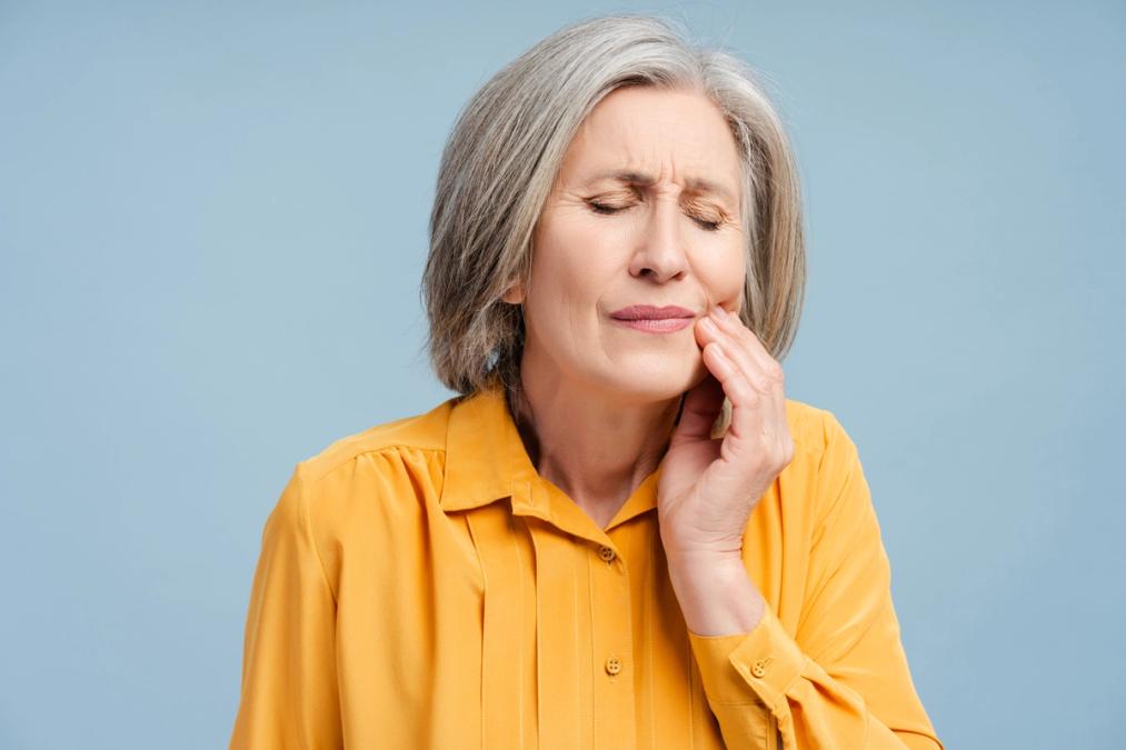 an elderly woman is holding her face in pain because of a toothache .