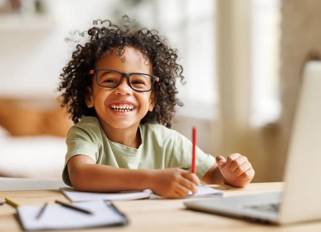 a young boy wearing glasses is sitting at a desk with a laptop .