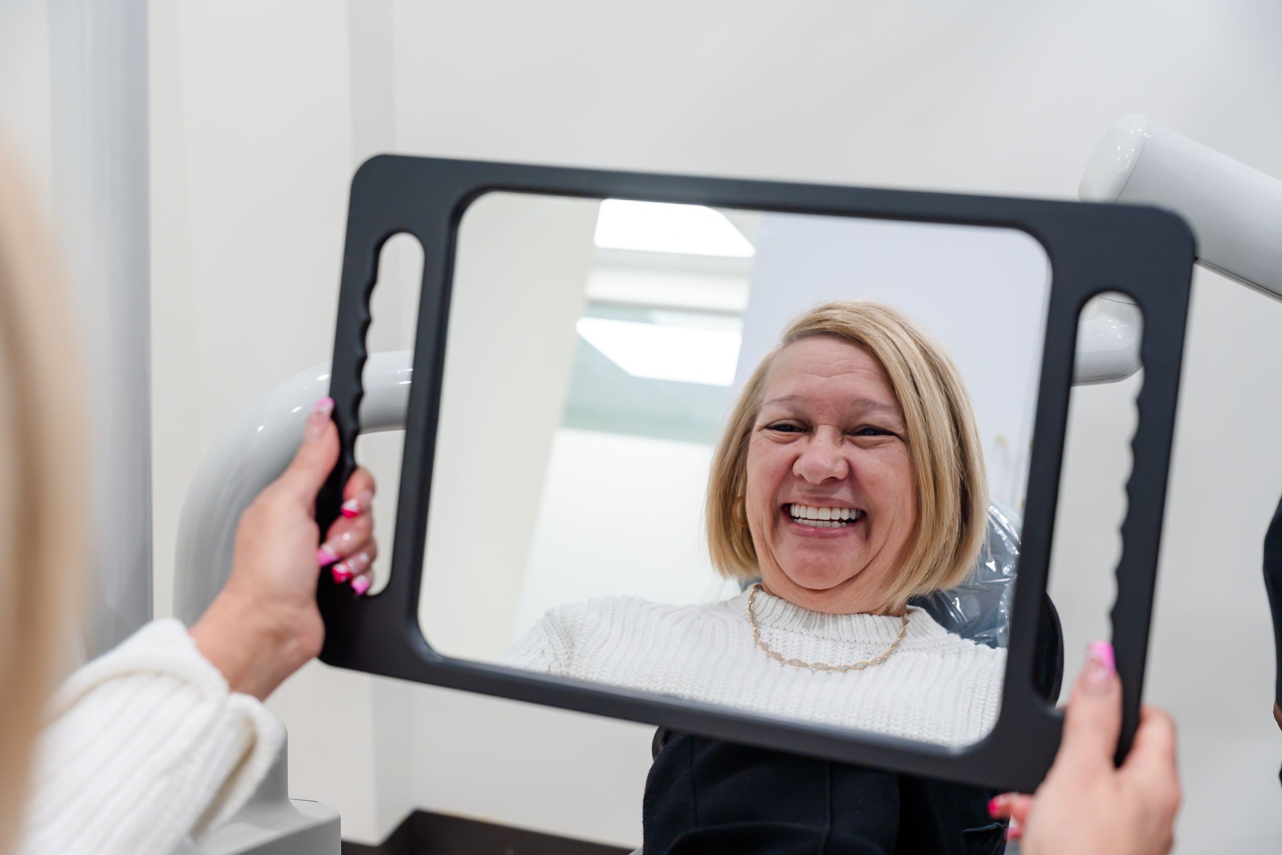 a woman is looking at her smile in a mirror .