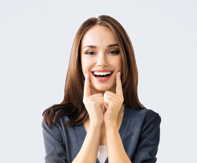 a woman is smiling and touching her face with her hands .