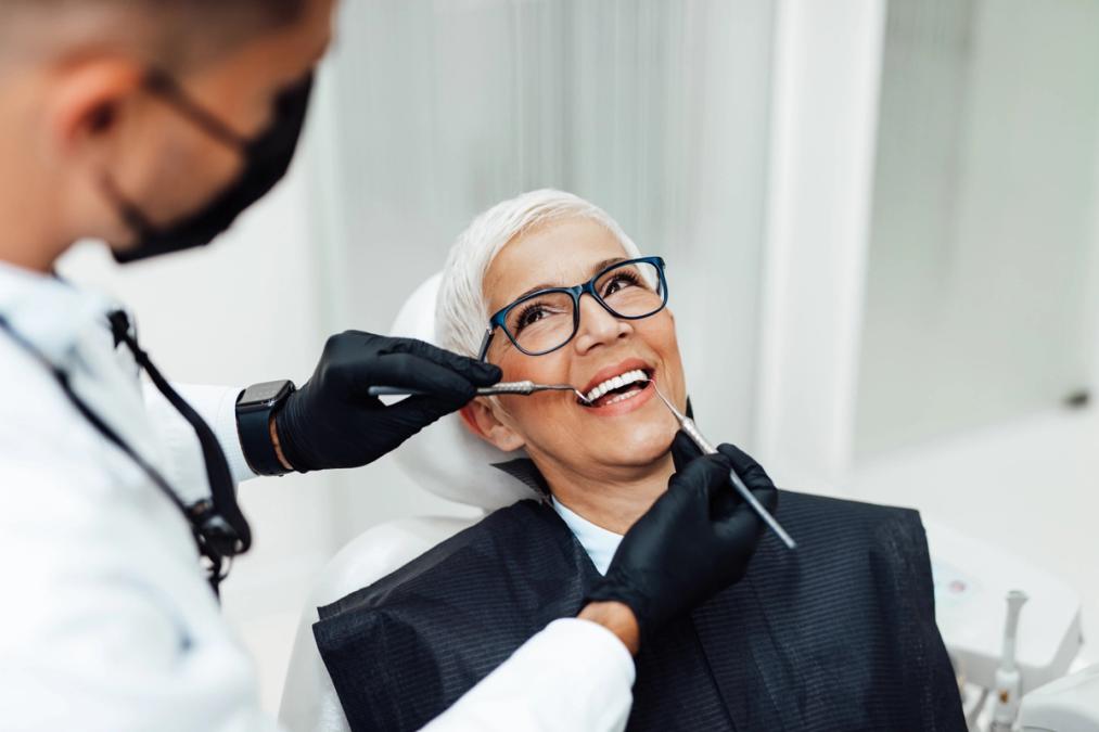 A dentist examines a smiling older woman's teeth.