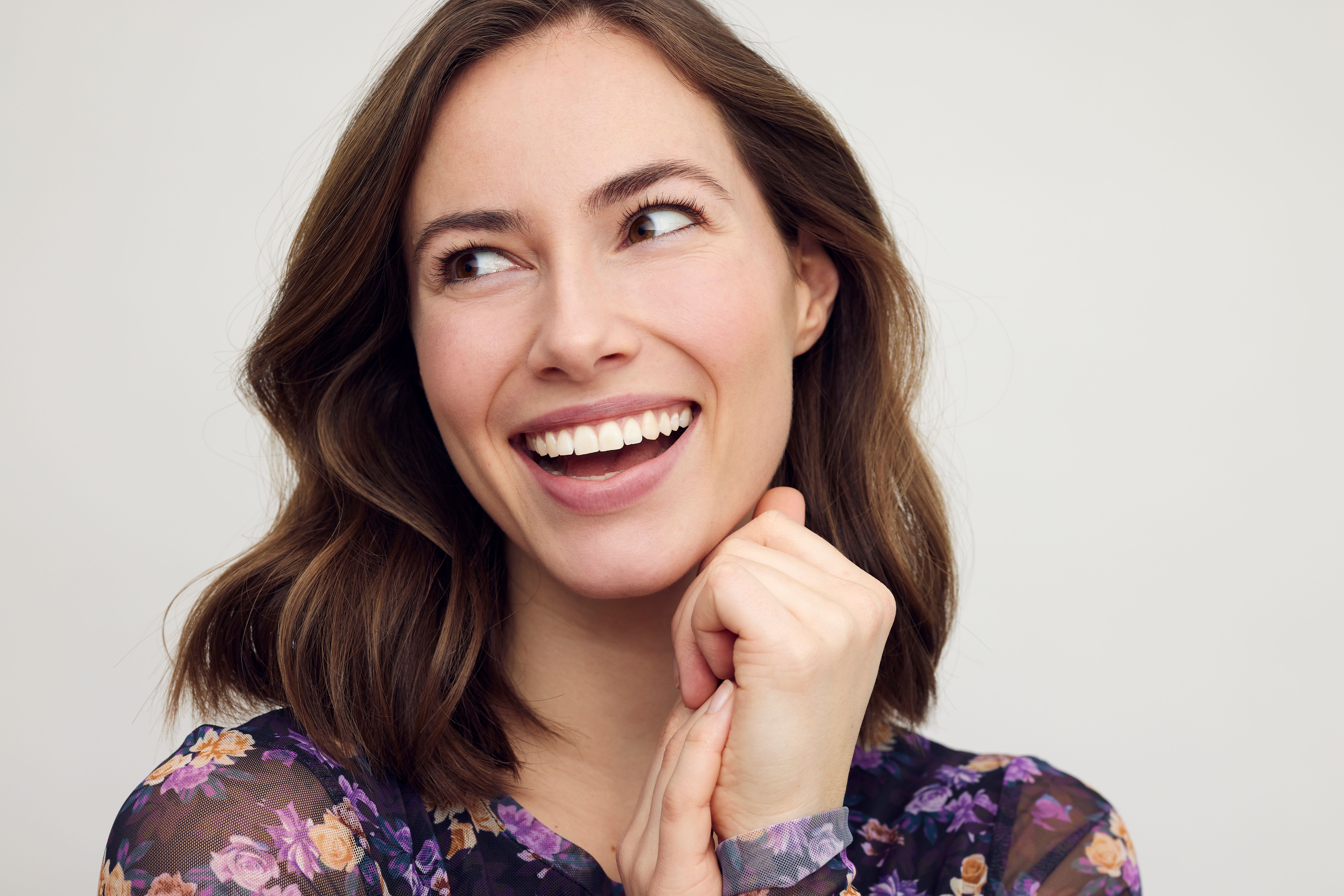 a woman in a floral dress is smiling with her hands on her chin .