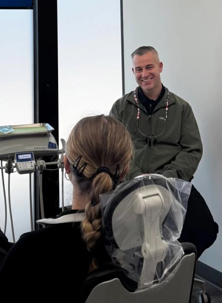 A smiling dentist looks at a patient from behind in a dental office.