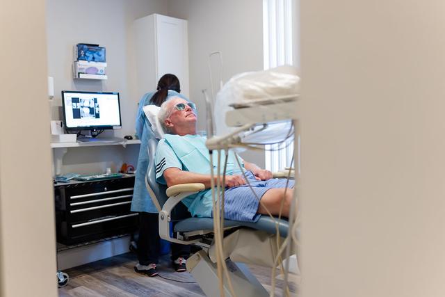 a man is sitting in a dental chair with a nurse behind him .