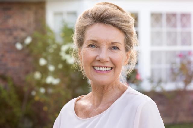 an elderly woman is smiling in front of a house .