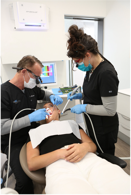 a woman is getting her teeth examined by two dentists