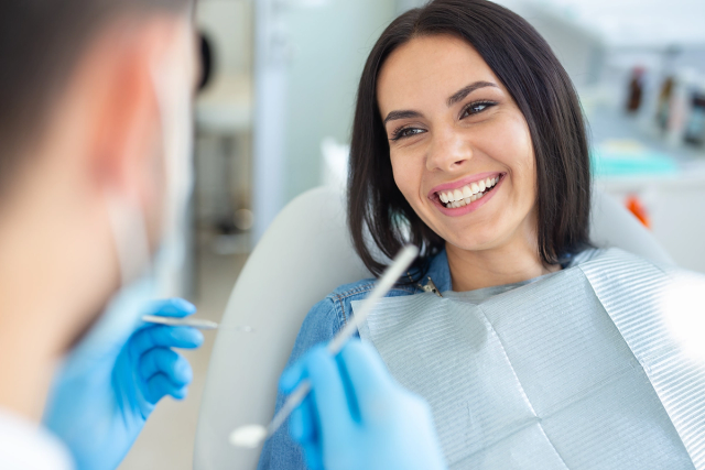 a woman in a dental chair smiles while a dentist examines her teeth