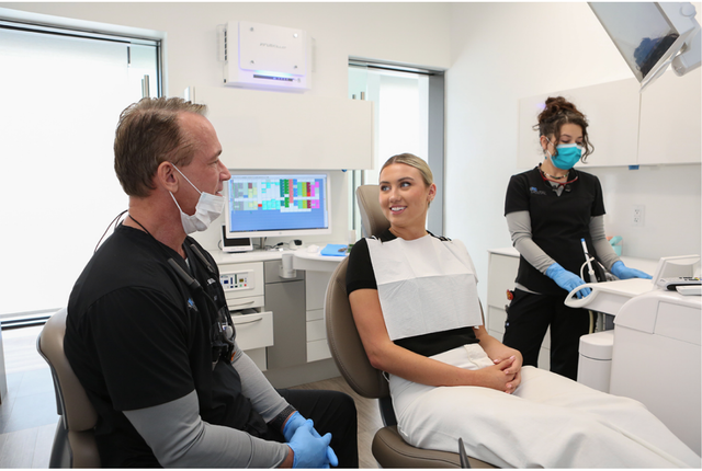 a woman is sitting in a dental chair talking to a dentist