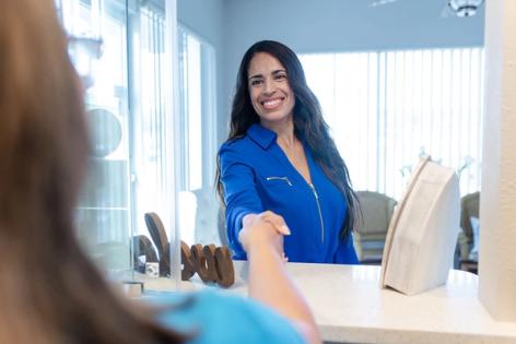 A smiling woman in a blue shirt shakes hands with another person across a counter.