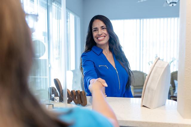 Smiling woman in a blue top shaking hands across a counter.