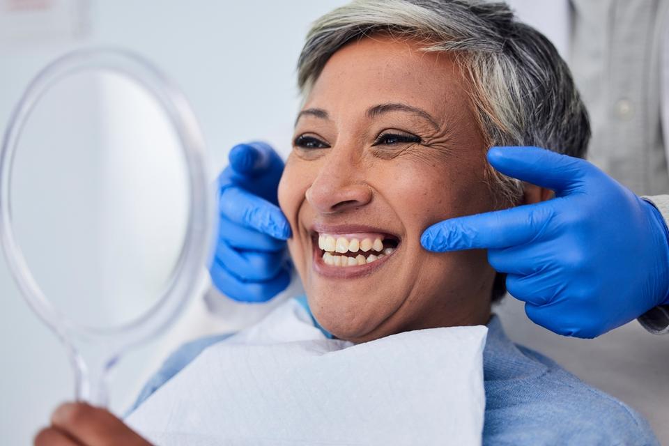 a woman is smiling while looking at her teeth in a mirror .