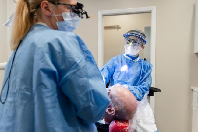Two dental professionals in full PPE treating a patient.