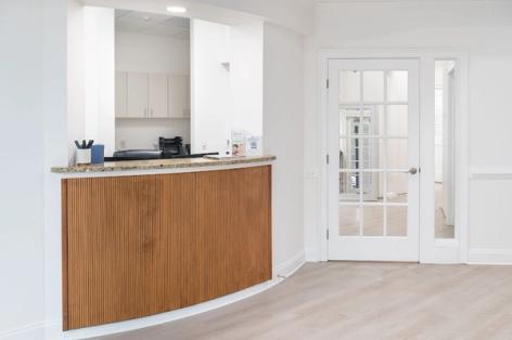 A clean, modern reception area with a curved wooden desk and a white glass-paneled door.