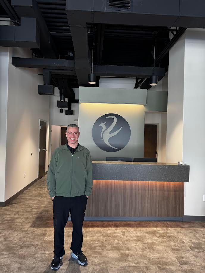 Smiling man in a modern office reception area with a logo behind the desk.