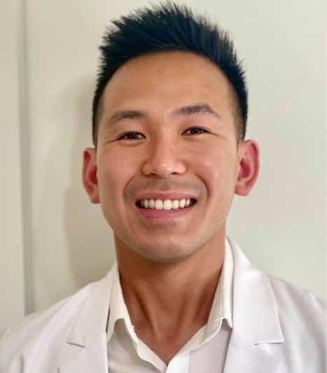 a man in a white coat is smiling for the camera .