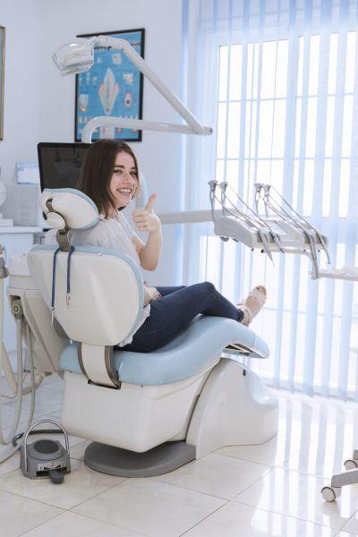 a woman is sitting in a dental chair and giving a thumbs up .