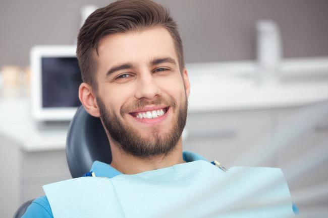 a man with a beard is smiling while sitting in a dental chair .