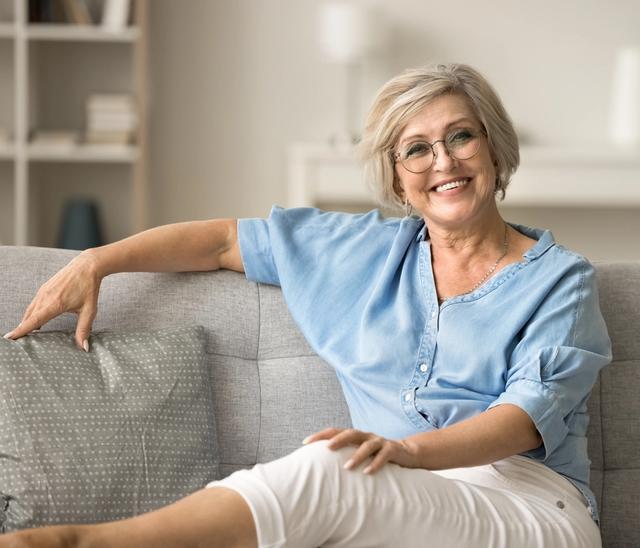 an older woman is sitting on a couch with her legs crossed and smiling .