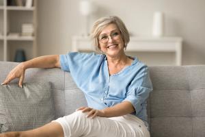 Smiling blonde woman with glasses sitting on a sofa.
