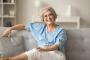 an older woman is sitting on a couch with her legs crossed and smiling.