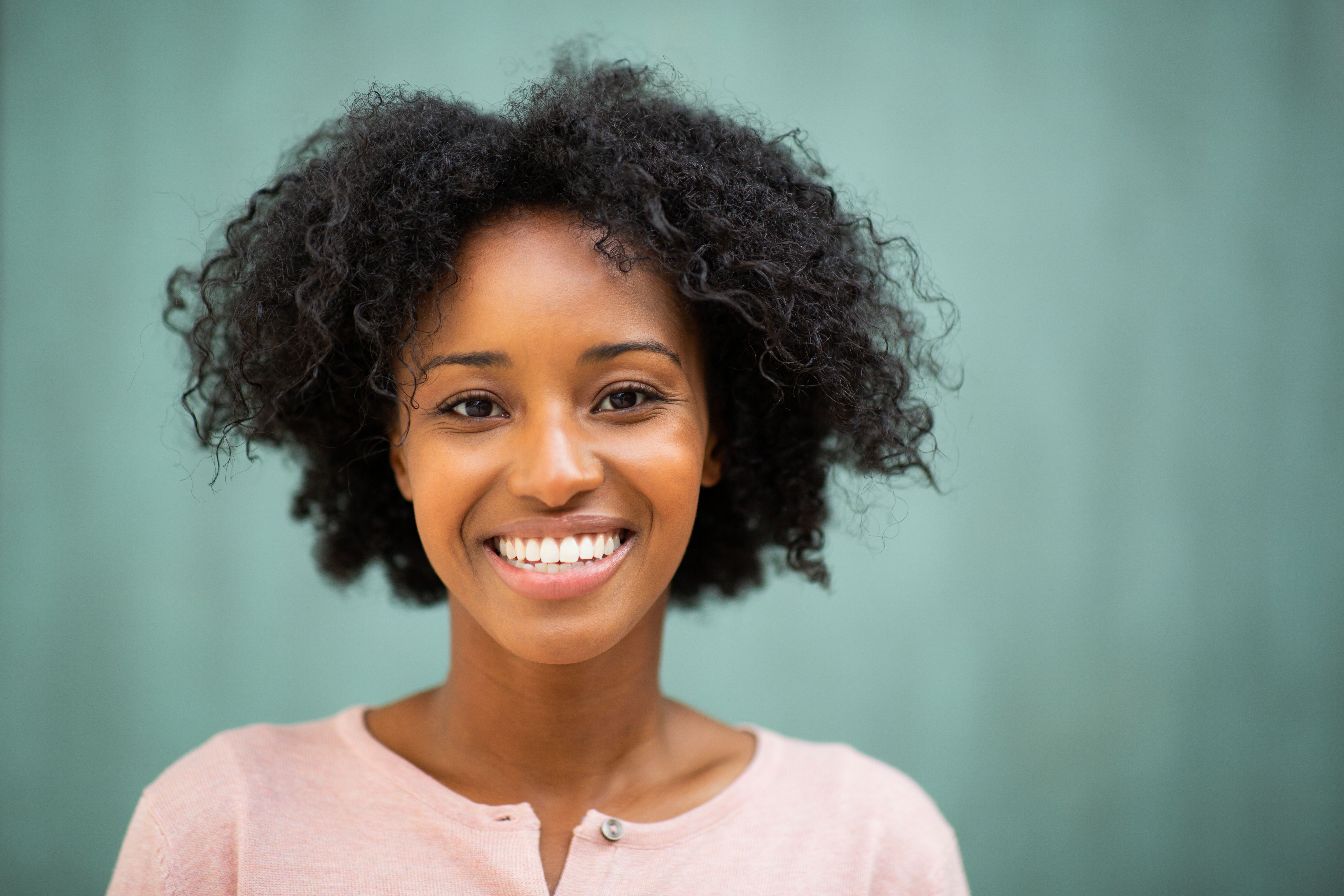 a woman with curly hair is smiling for the camera .