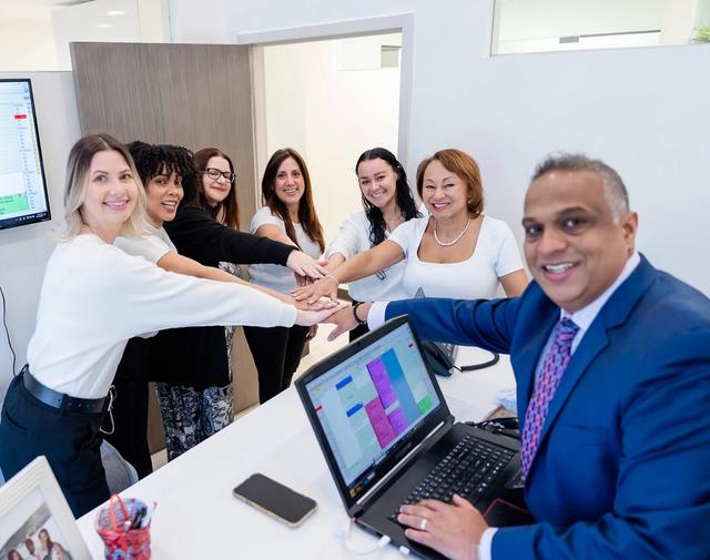 a group of people are putting their hands together in front of a laptop computer .