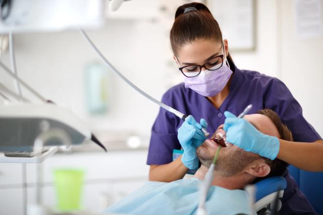 a female dentist is examining a man 's teeth in a dental office .