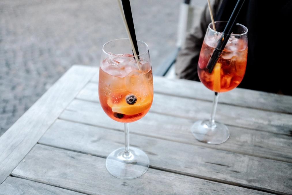two glasses of cocktails with straws on a wooden table .