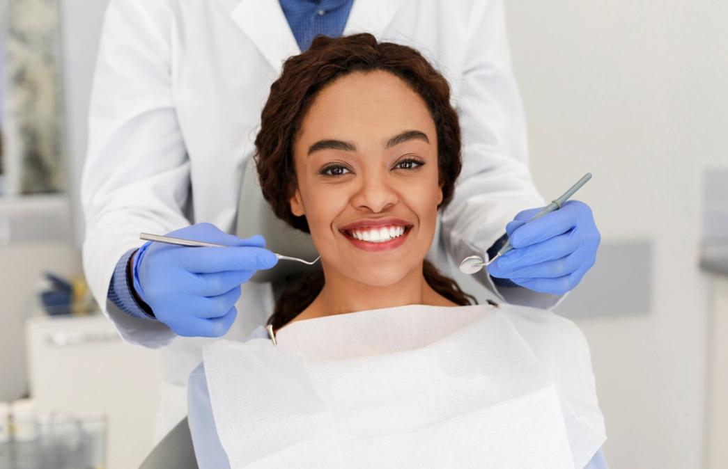 Smiling Black woman in a dental chair with a dentist holding dental tools.