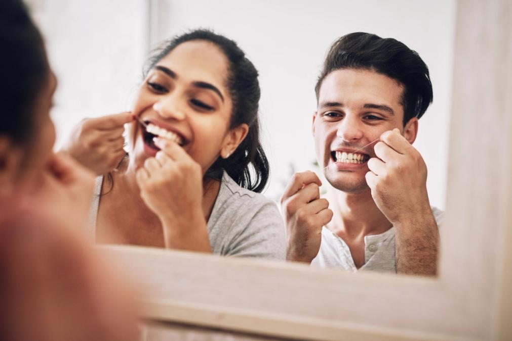 a man and a woman are flossing their teeth in front of a mirror .