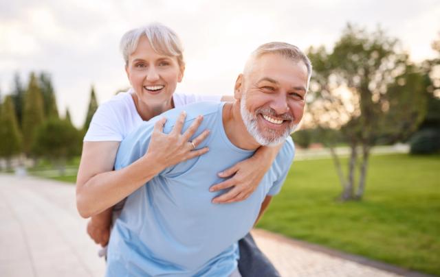 a man is giving a woman a piggyback ride in a park .