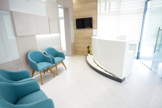 a waiting room with blue chairs and a white counter in a dental office .