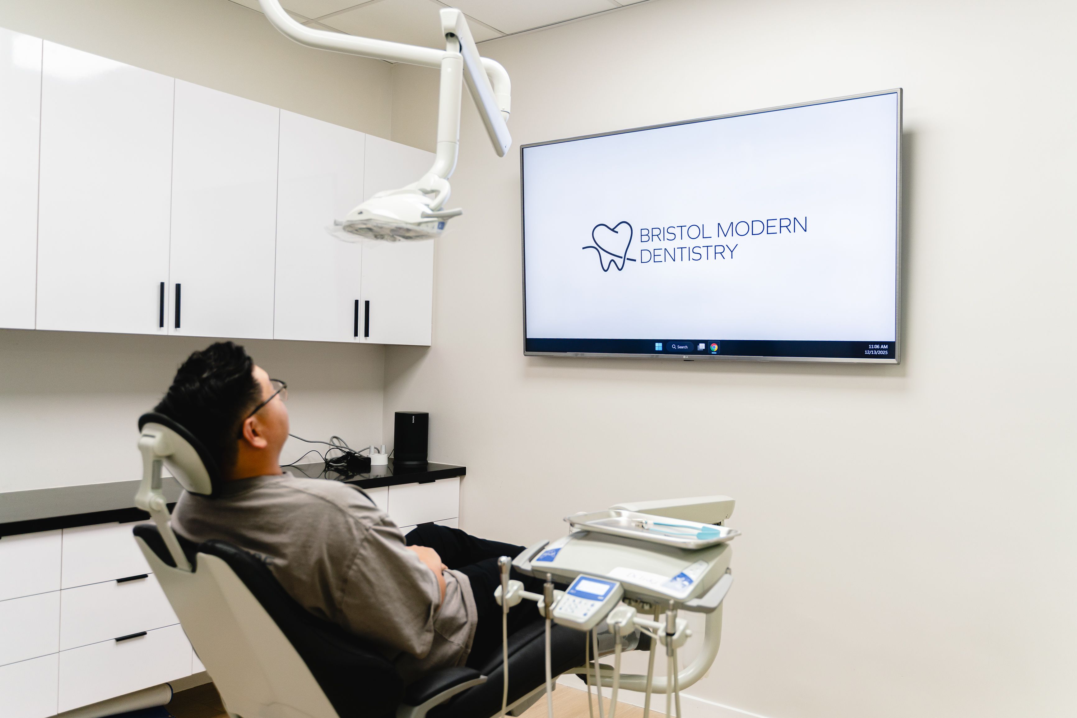 A person sits in a dental chair looking at a TV screen displaying the "Bristol Modern Dentistry" logo in a modern dental office.