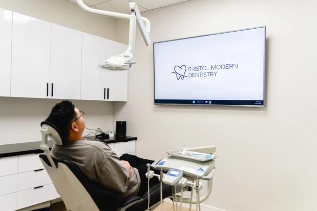 Patient in a modern dental chair looks at a TV displaying the 'Bristol Modern Dentistry' logo.