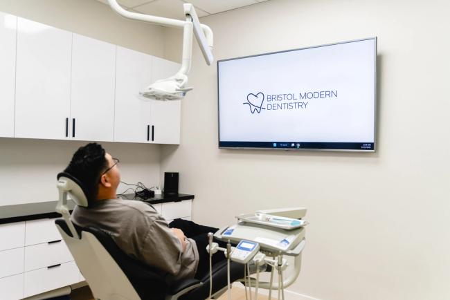 Patient in a modern dental chair looks at a TV displaying the 'Bristol Modern Dentistry' logo.