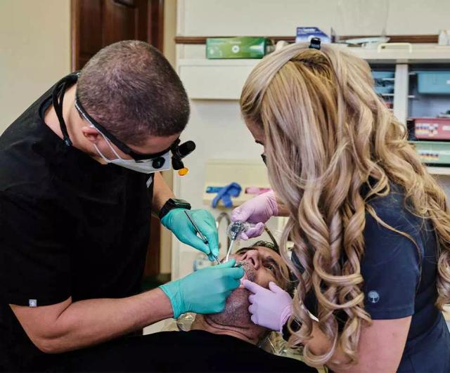 a man is getting his teeth examined by a dentist and a nurse in a dental office .