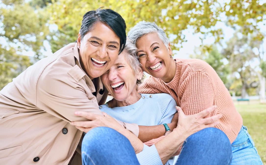 Three diverse women joyfully hugging and laughing in a park.