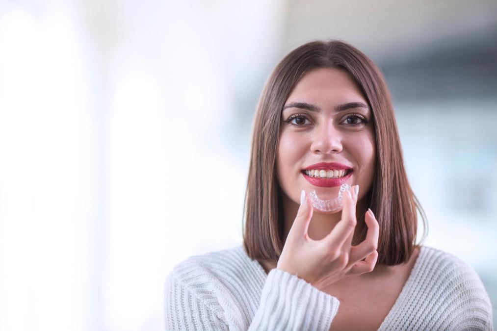 Smiling woman holding a clear dental aligner.