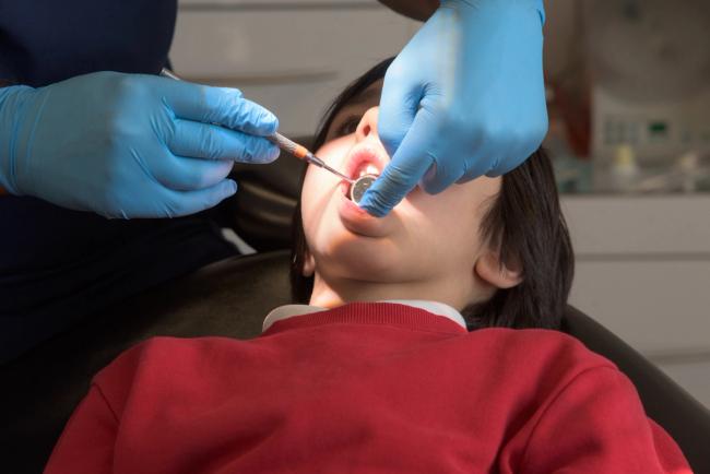 A child with an open mouth is examined by a dentist wearing blue gloves and using dental instruments.