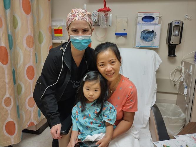 a woman wearing a mask is standing next to a little girl in a hospital bed .