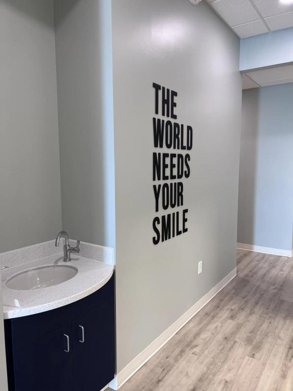 a bathroom with a sink and a sign on the wall that says `` the world needs your smile '' .