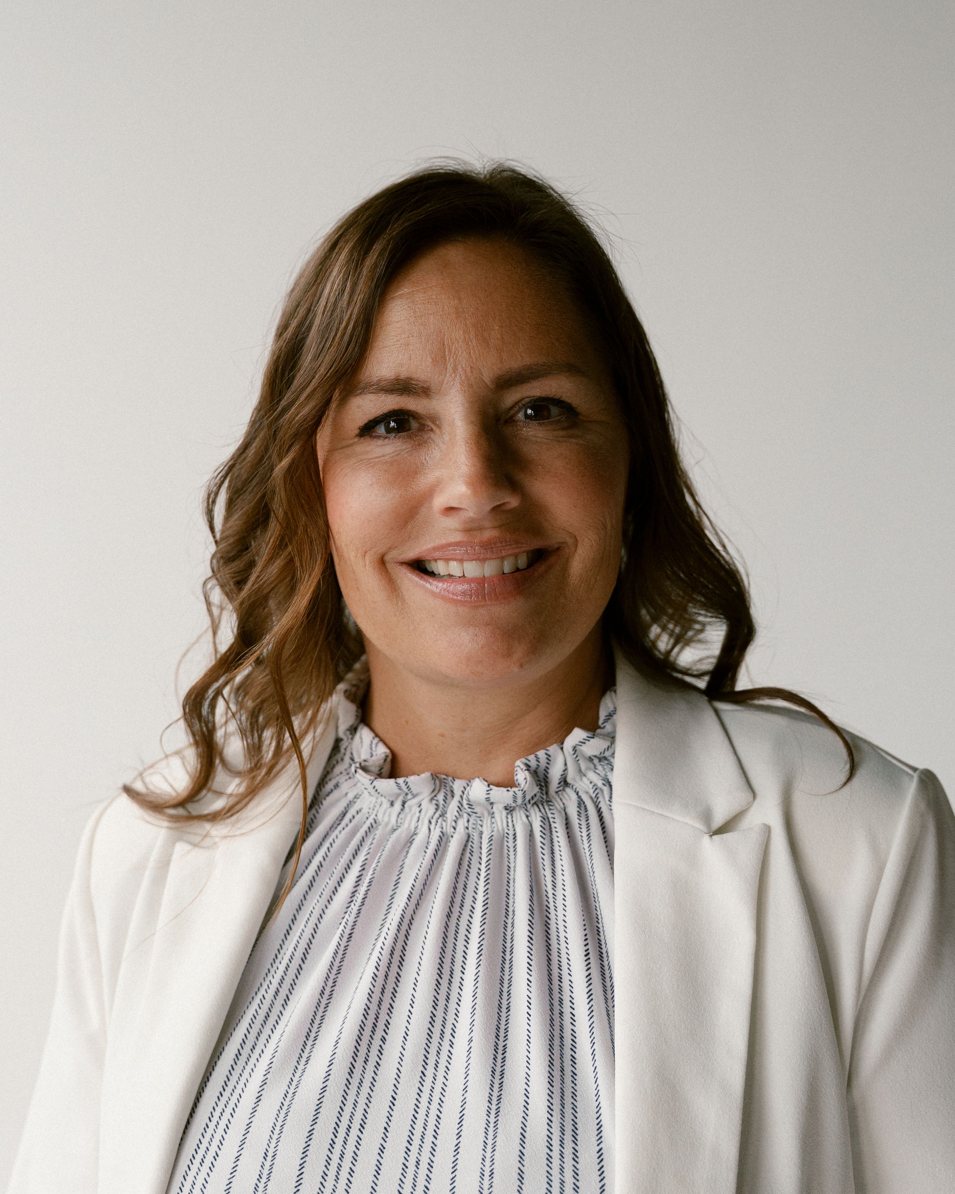 a woman wearing a white jacket and striped shirt smiles for the camera
