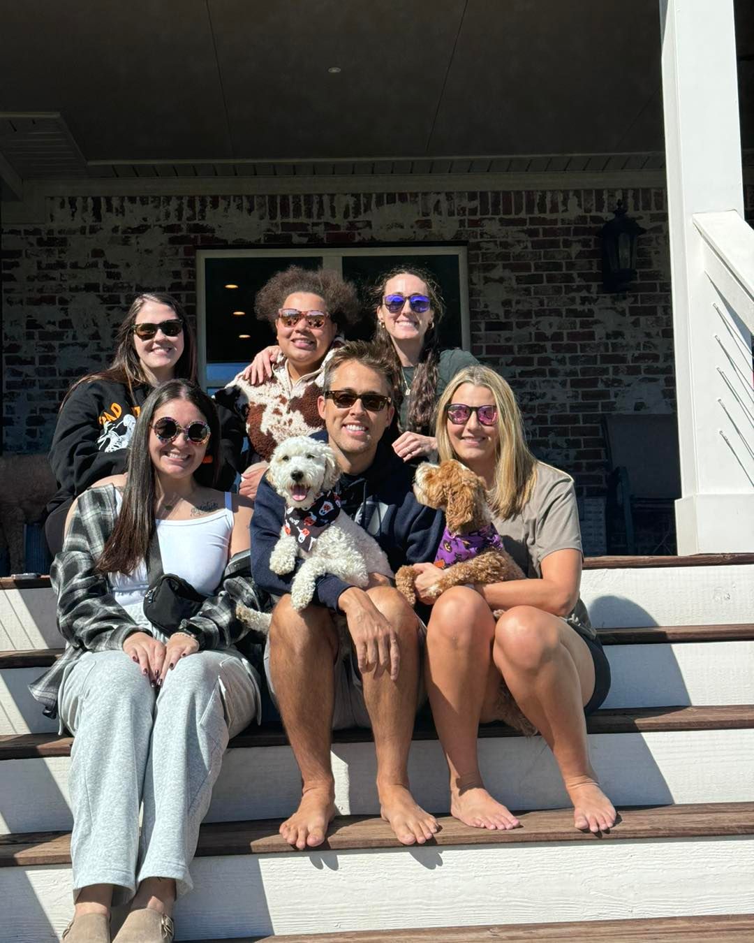 a group of people sitting on the steps of a house with their dogs
