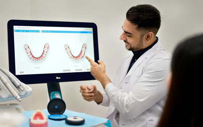 a dentist is pointing at a computer screen while talking to a patient .