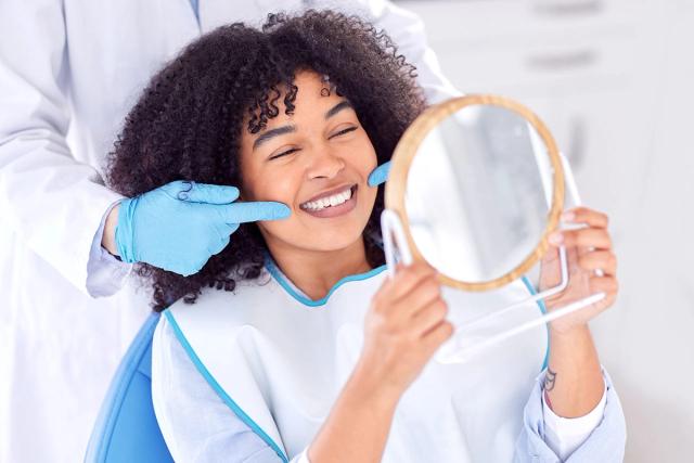 a woman is sitting in a dental chair looking at her teeth in a mirror .