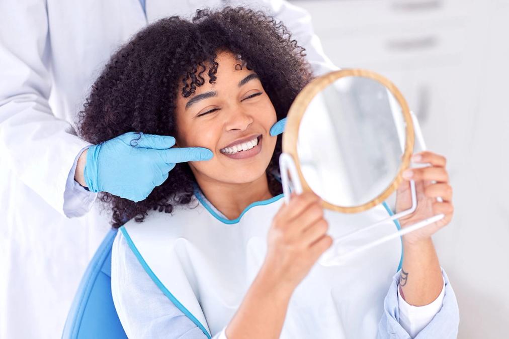 a woman is sitting in a dental chair looking at her teeth in a mirror .