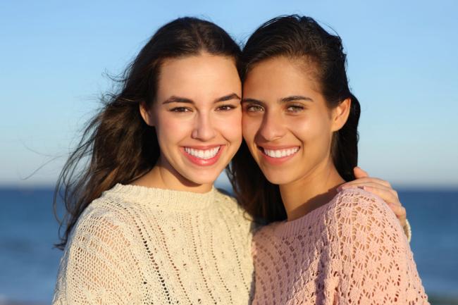 two young women are posing for a picture together on the beach .