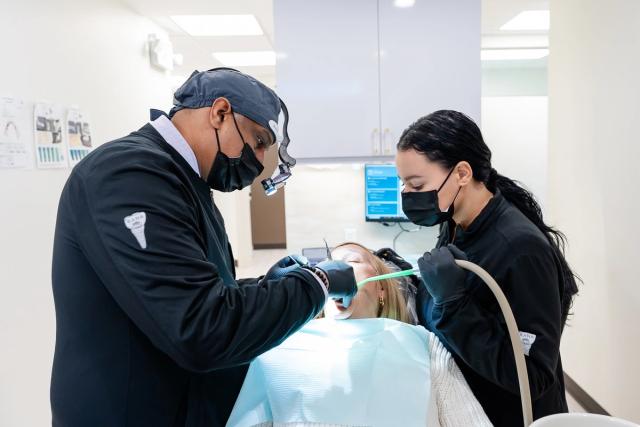 a dentist and a dental assistant are examining a patient 's teeth in a dental office .